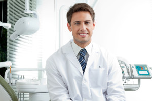 Portrait of happy male dentist wearing lab coat while sitting in clinic