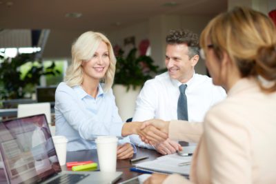 Shot of a business woman shaking hands with smiling woman while consulting with customers.