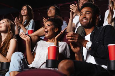 Multiethnic happy audience clapping hands while sitting at the cinema and watching movie