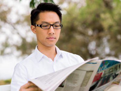 Young casually dressed businessman reading a newspaper in park