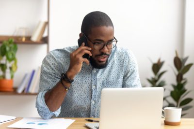Serious african-american employee making business call focused on laptop at workplace. Black businessman consulting customer, discussing financial report. Contract negotiation and discussion concept