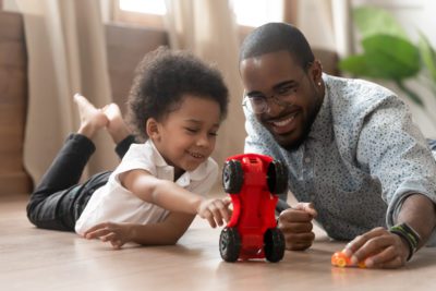 Cute little african kid son play toy cars with black dad, happy family small mixed race son and loving young father babysitter having fun racing on warm floor at home, family daddy child leisure game