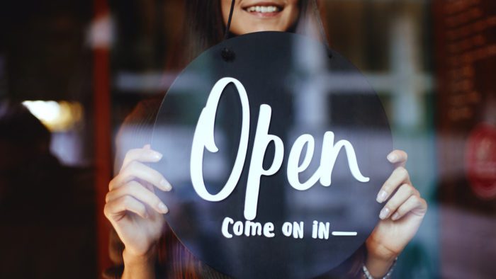 woman flipping sign in business window to show open